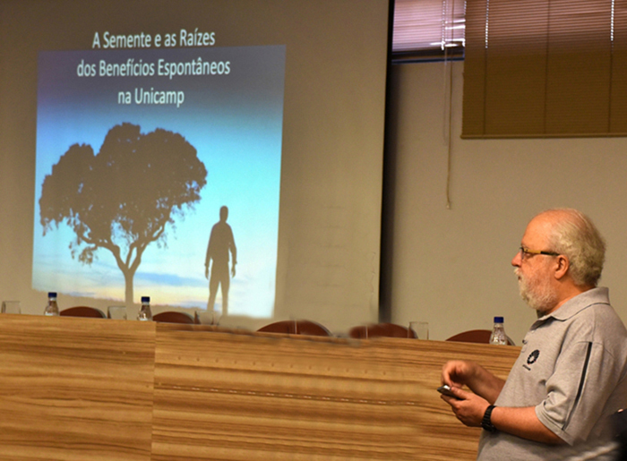 Reitor Tadeu ao lado de apresentação de slide durante discursode abertura do evento de 10 anos do GGBS