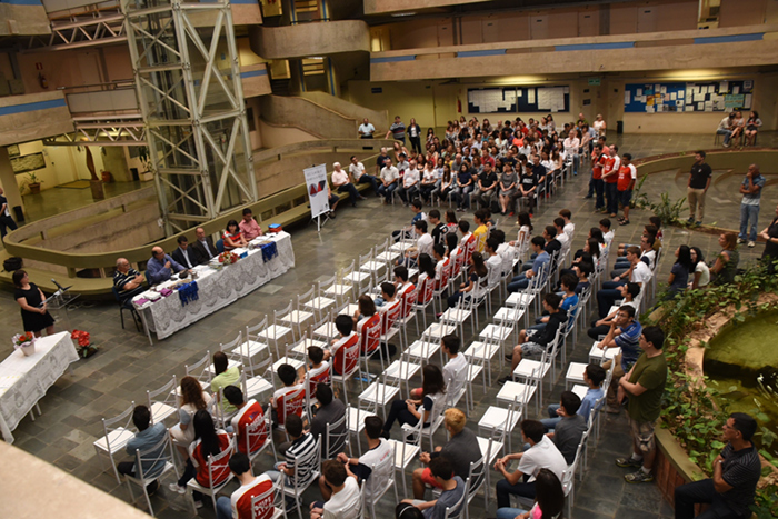 Vista do alto, de participantes e convidados do evento de premiação da 32ª Olimpíada de Matemática da Unicamp, com cerca de 130 pessoas, e à frente a mesa diretora dos trabalhos, composta por seis pessoas