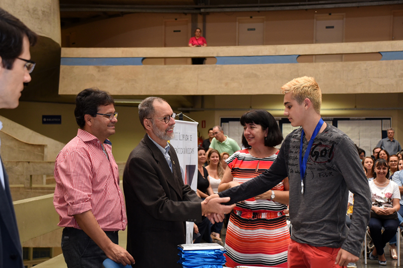 Um jovem, à direita, é cumprimentado com aperto de mão pelo professor João Frederico da Costa Azevedo Meyer, à esquerda, após receber medalha como premiação na 32ª OMU