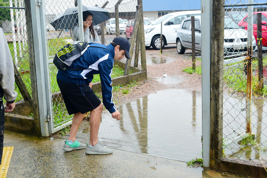 Homem inclinado para frente observa grande poça d'água formada a sua frente, no local de passagem por portão