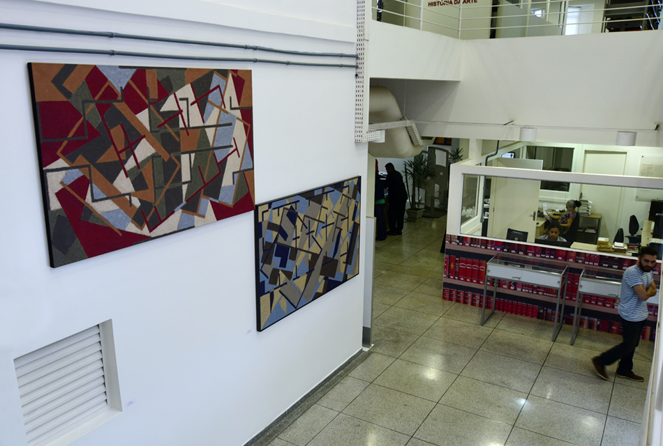 Vistas de uma espécie de mezanino, duas telas em exposição, medindo cerca de 2 metros por 1 metro, na horizontal, com pintura de figuras geométricas abstratas em tons vermelhos e azuis, sendo que ambas estão fixadas uma parede