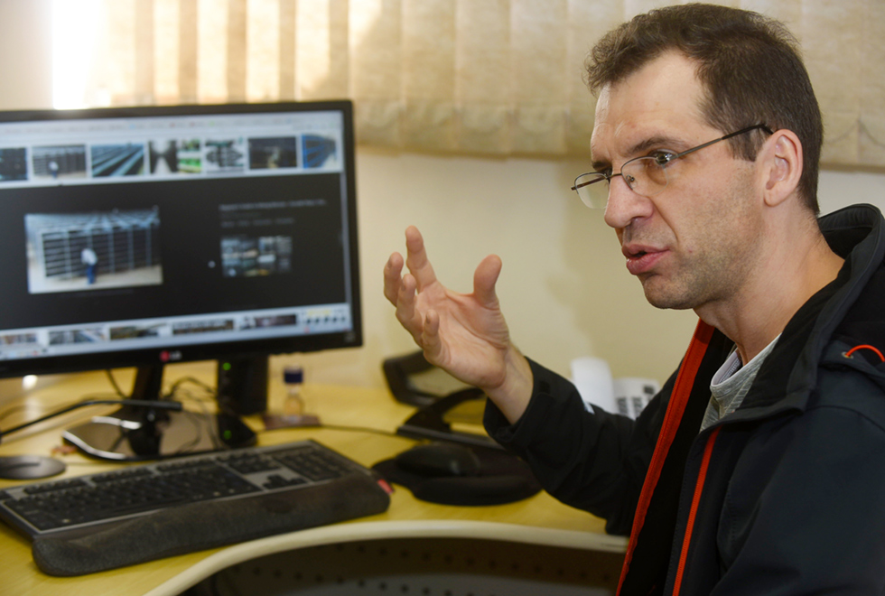 A galeria mostra o professor Serguei Popov, do Instituto de Matemática, Estatística e Computação Científica (Imecc) da Unicamp, um dos criadores da criptomoeda Iota. Para acessá-la, tecle enter. Audiodescrição: Num ambiente interno no fundo parede cinza persianas marrom claro. Parte de uma mesa nela um computador ligado na tela uma foto de uma pessoa e uma prateleira. Sentado a mesa uma pessoa usando óculos braço direito levantado  sua mão espalmada. Veste camiseta cinza jaqueta preta com zíper vermelho.   