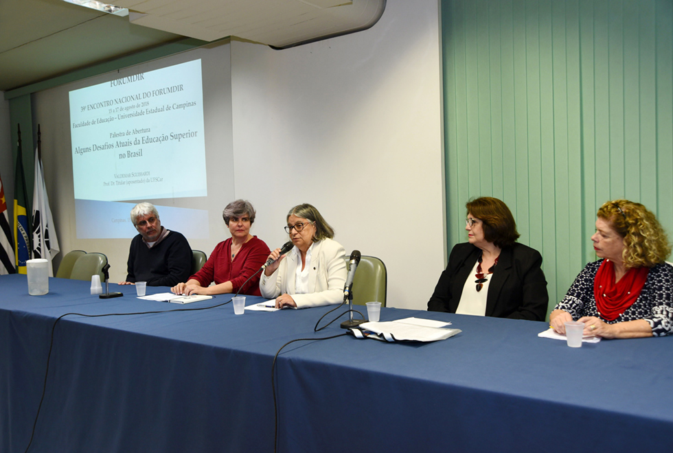 A galeria mostra o 39º Encontro Nacional do Fórum Nacional de Diretores d Faculdades. Para acessá-la, tecle enter. Audiodescrição: Ambiente interno, no fundo parede branca nela persiana aberta verde claro. Material projetado na parede. Parte três bandeiras, persiana fechada. A frente mesa retangular azul. Cinco pessoas sentadas a mesa, direita para esquerda, terceira pessoa usando óculos segura com a mão direita microfone. Sua mão esquerda sobre papéis na mesa. Os demais prestam atenção na terceira pessoa.