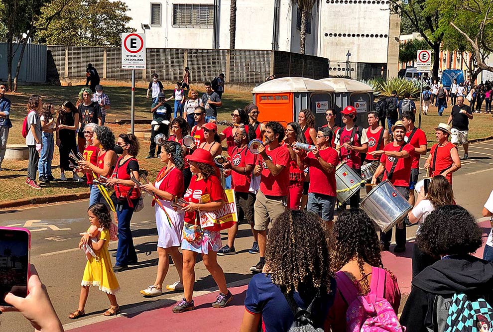 imagem colorida, visitantes assitindo apresentação de uma bateria pelo campus